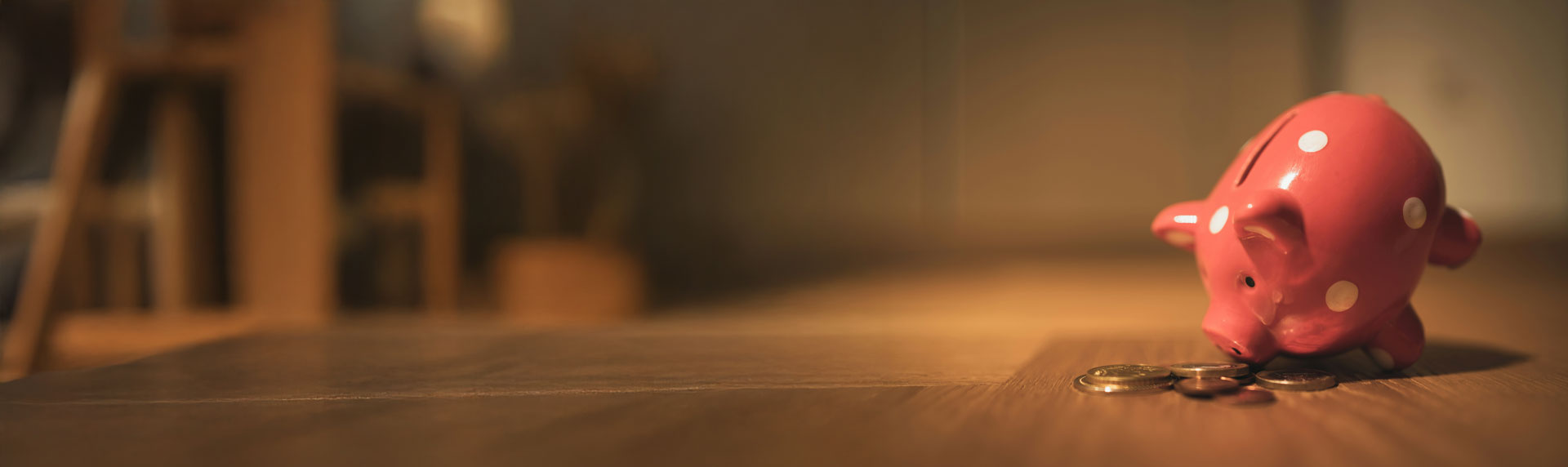 picture of a piggy bank on a wooden surface near some loose coins.